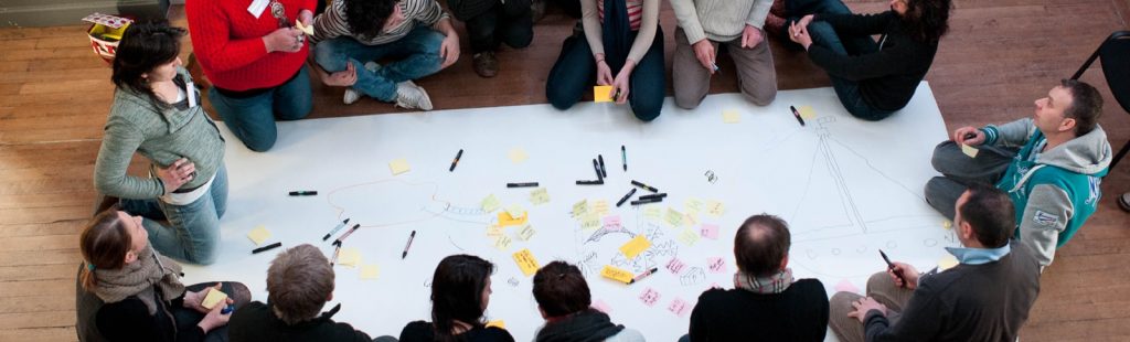 Plusieurs personnes rassemblées autour d'une grande feuille avec post-it et stylos.